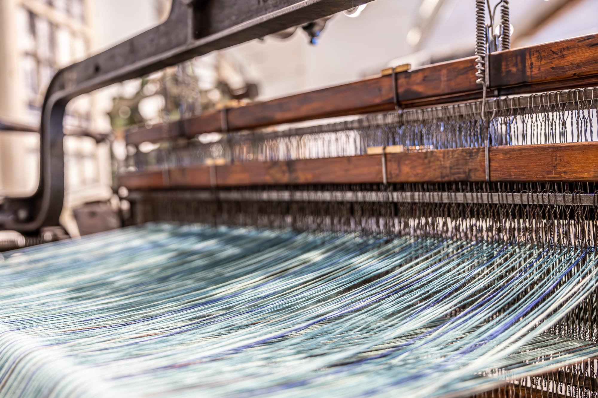 Photo of an old loom in action with a wide expanse of threads in pale blues and greens